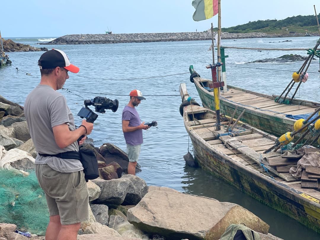 Crew filming near the breakwater and moored canoes in Dixcove